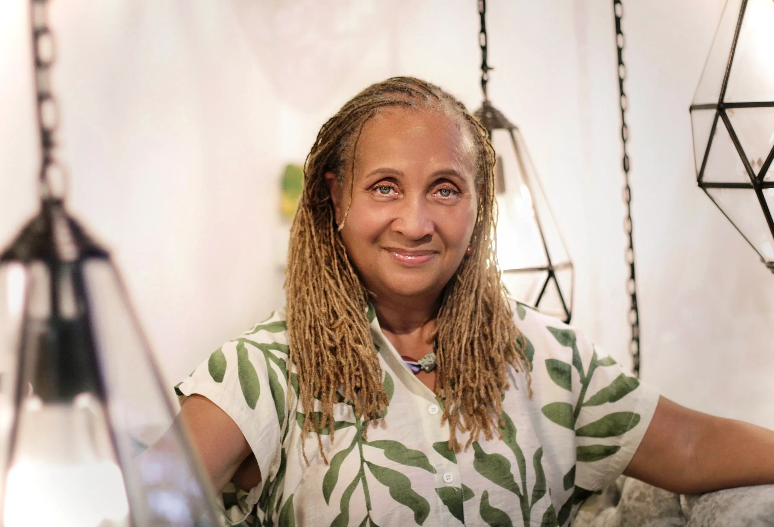 Smiling woman with braided hair wearing a leafy patterned shirt.